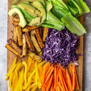 Sliced vegetables arranged on a large wooden cutting board on top of a granite surface
