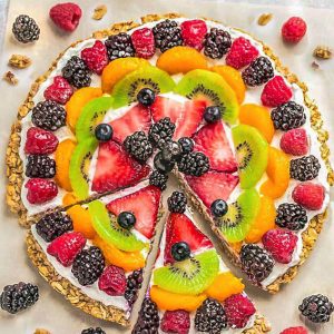 Top view of Healthy Fruit Pizza on parchment paper with 2 sices cut
