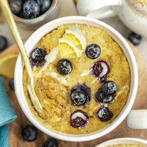 Top view of blueberry mug cake in white bowl with fresh lemons and blueberries.