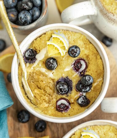 Top view of blueberry mug cake in white bowl with fresh lemons and blueberries.