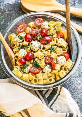 Top view of gluten free caprese pasta salad in a clear mixing bowl with two wooden spoons