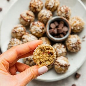 A hand holding one vegan energy ball over a plate