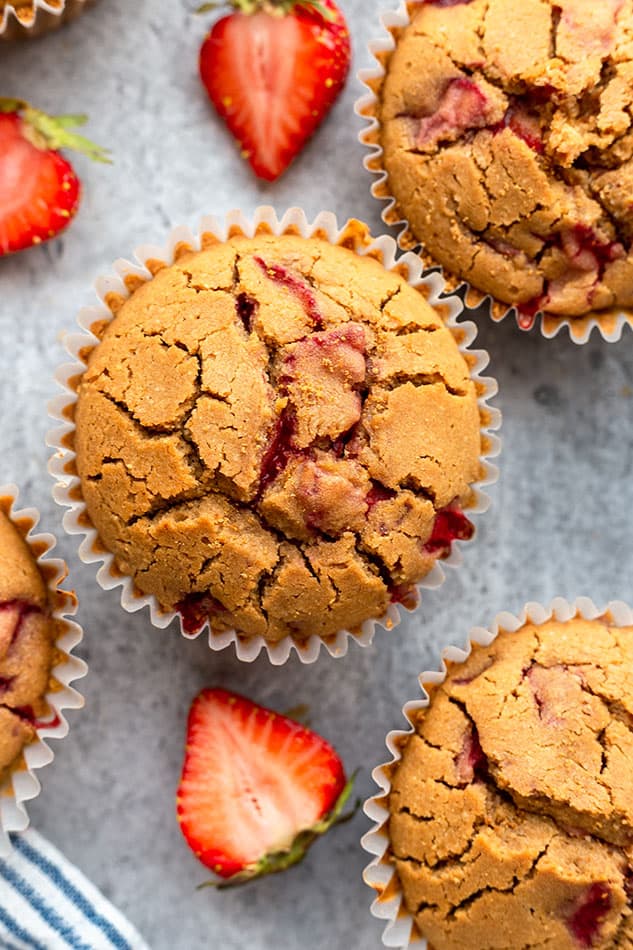 Overhead image of strawberry muffin on grey surface with fresh strawberries.