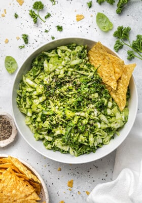 Overhead shot of a crunchy green cabbage salad in a white bowl with tortilla chips on the side