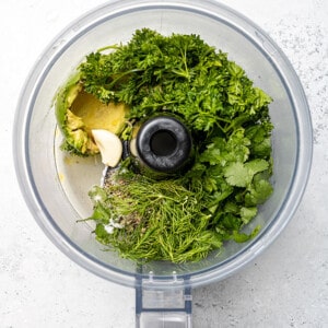 Top view of ingredients to make green goddess dressing in a food processor bowl