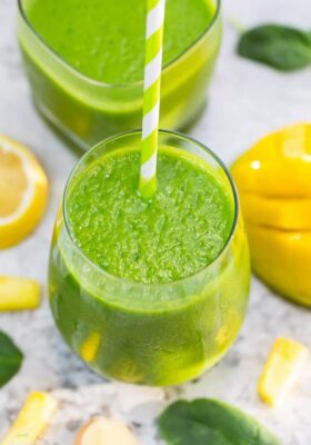 Top view of one healthy spinach smoothie in a clear glass with a straw on a grey marble background with fruit