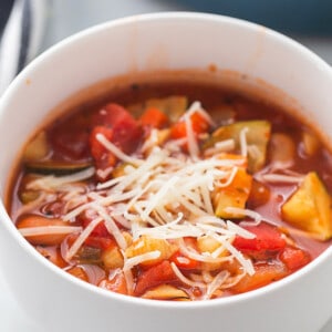 Close-up of a serving of vegan minestrone soup in a white bowl with grated cheese