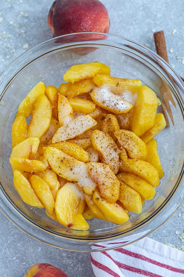 Overhead image of fresh peaches covered in cinnamon in glass bowl.