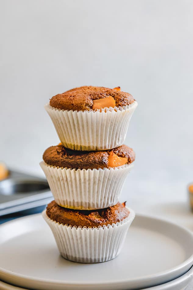 Three Paleo Peach Muffins stacked on a white plate