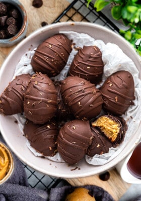 A grey bowl filled with 10 chocolate peanut butter eggs and one has a missing bite