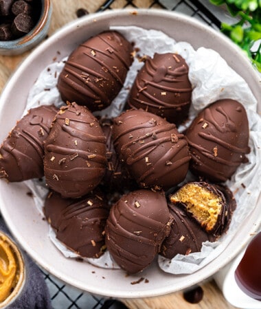 A grey bowl filled with 10 chocolate peanut butter eggs and one has a missing bite