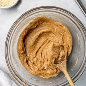 Cashew butter mixed with maple syrup, vanilla and protein powder in a clear with a wooden spoon