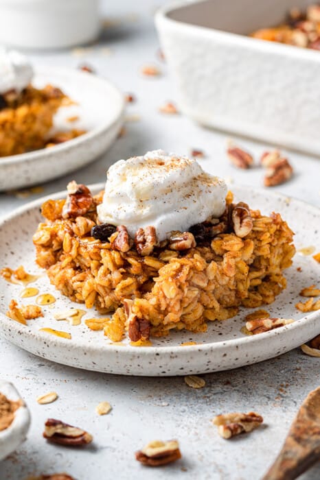Side view of a square of vegan pumpkin baked oatmeal on a white plate with a dollop of vegan yogurt