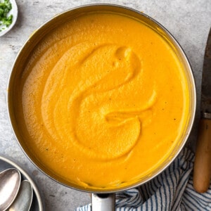 A Pot of Creamy Pumpkin Soup Shown From Above with a Bowl and Two Spoons Beside It
