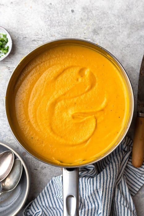 A Pot of Creamy Pumpkin Soup Shown From Above with a Bowl and Two Spoons Beside It