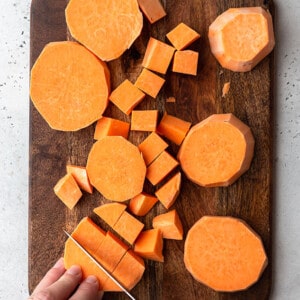 Process shot: A hand cutting sweet potatoes on a wooden cutting board