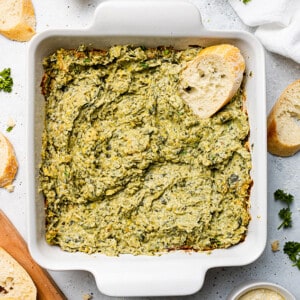 Creamy Vegan Spinach Artichoke Dip in a white square baking pan with a toasted baguette