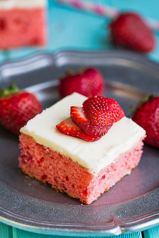 A square of frosted strawberry cake on a metal plate