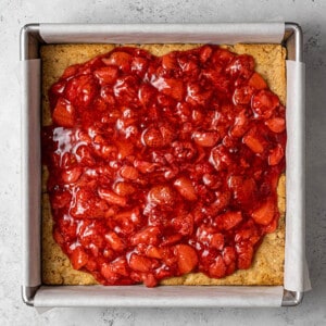 Strawberry filling layered on the shortbread crust for strawberry pie bars in a square baking pan