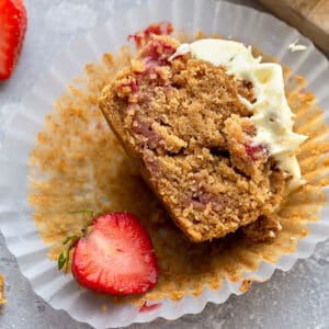 Top close-up view of one half of a healthy strawberry muffin topped with whipped coconut cream on a grey background