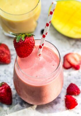 Top view of one healthy strawberry smoothie in a clear glass with a straw on a grey marble background with fruit