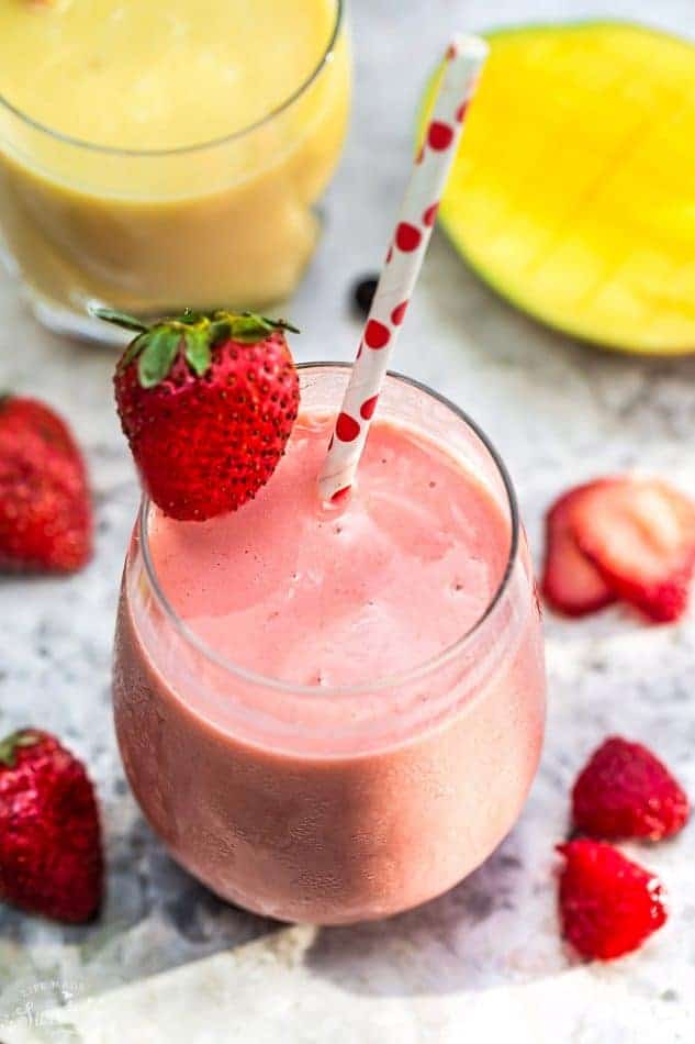 Top view of one healthy strawberry smoothie in a clear glass with a straw on a grey marble background with fruit for berry recipes.