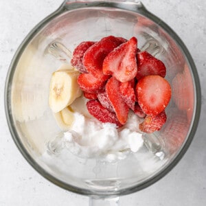 Frozen strawberries, ripe banana, coconut cream, nut butter and dairy-free milk inside of a high-speed blender