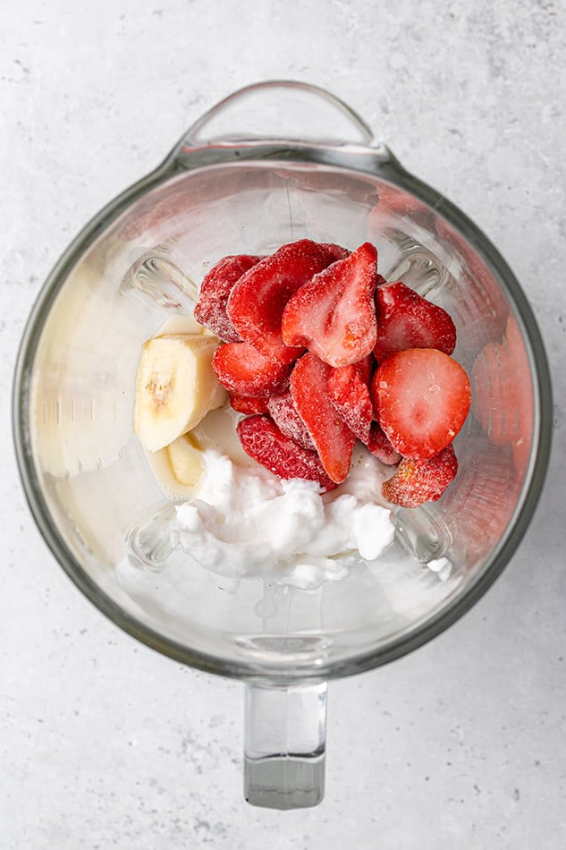 Frozen strawberries, ripe banana, coconut cream, nut butter and dairy-free milk inside of a high-speed blender