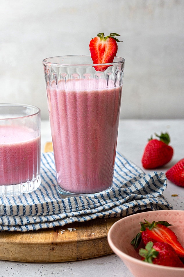 A strawberry smoothie in a glass on a cutting board beside a bowl of fresh berries
