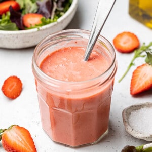 45 degree shot of strawberry vinaigrette dressing in a small jar with a spoon