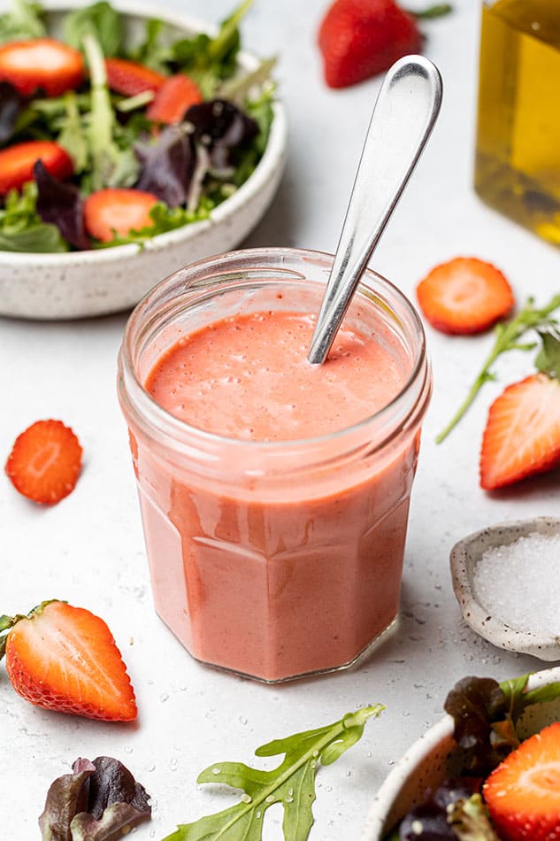 45 degree shot of strawberry vinaigrette dressing in a small jar with a spoon