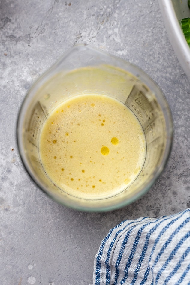 Overhead view of a liquid measuring cup of dressing for Tomato Cucumber Salad