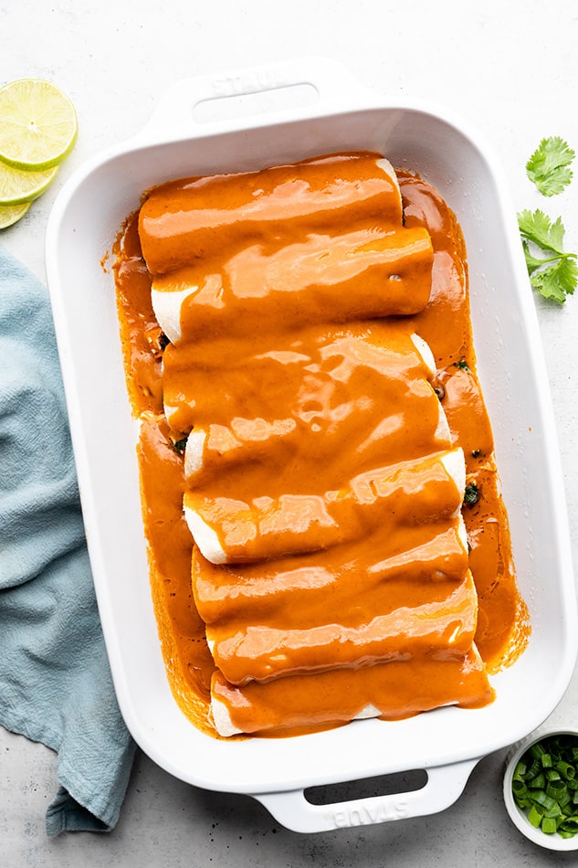 The overhead view of vegetarian enchiladas lined up in a baking dish and covered with sauce