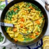Vegetable noodle soup in a blue dutch oven / pot with a soup ladle
