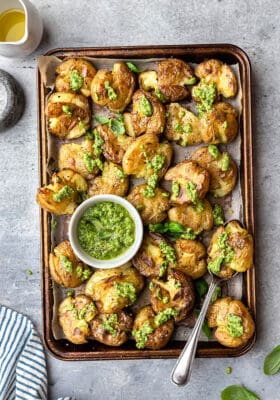 Top view of crispy smashed potatoes with pesto on a baking sheet