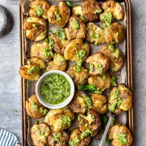 Top view of crispy smashed potatoes with pesto on a baking sheet