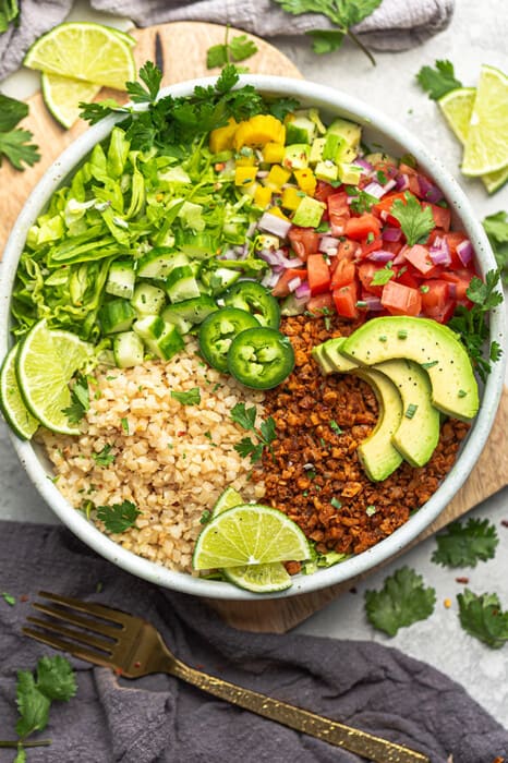 A close-up shot of a vegan taco bowl topped with jalapeño slices and lime wedges