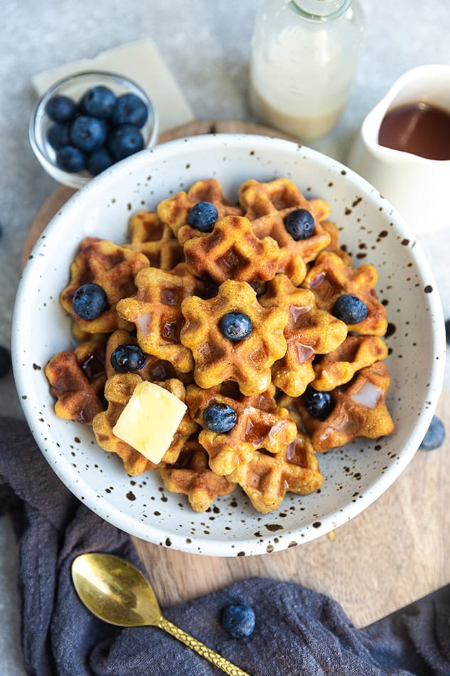 Waffle cereal topped with blueberries, syrup, and butter with milk on the side.