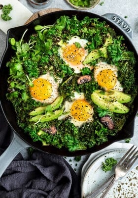 Top view of healthy green shakshuka in a grey cast-iron skillet on a grey background with forks