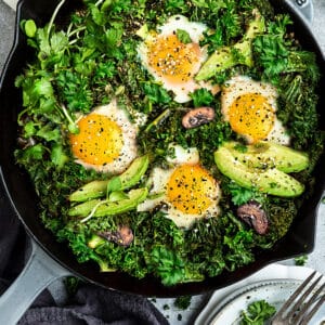Top view of healthy green shakshuka in a grey cast-iron skillet on a grey background with forks