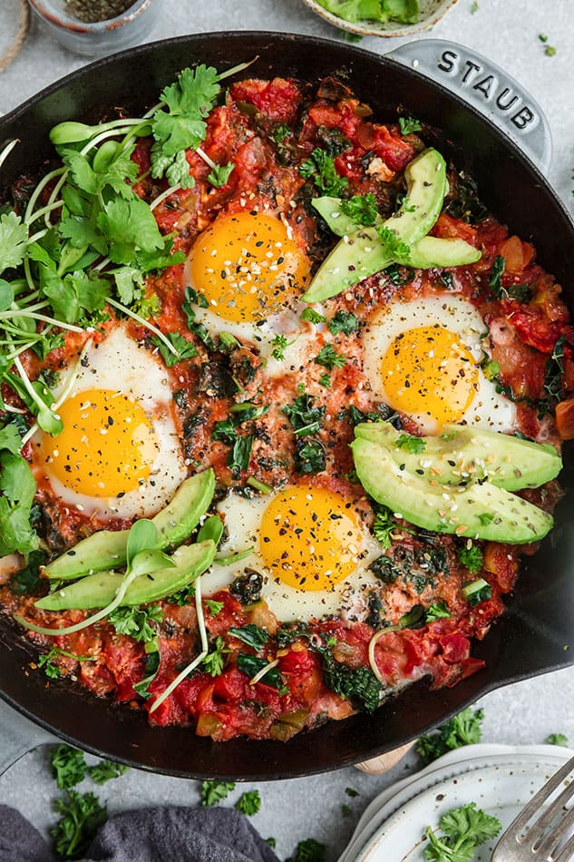 Overhead image of traditional shakshuka with eggs and avocado.