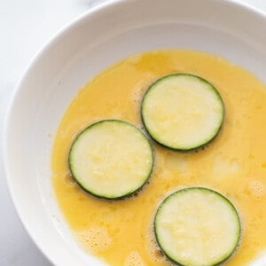 Three sliced zucchini rounds in a bowl of beaten eggs