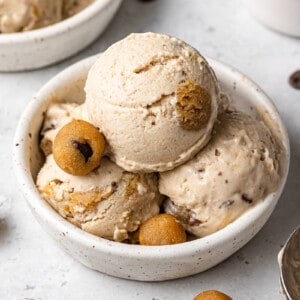 Side view of a three scoops of cookie dough ice cream in a white bowl with cookie dough chunks