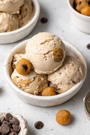 Side view of a three scoops of cookie dough ice cream in a white bowl with cookie dough chunks