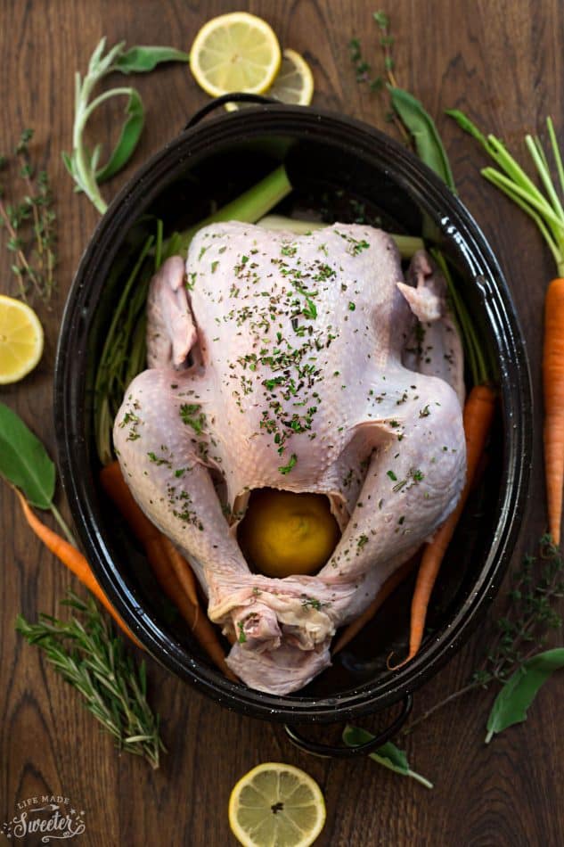Top view of a Raw Whole Turkey in a black roasting pan with carrots, lemon and herbs