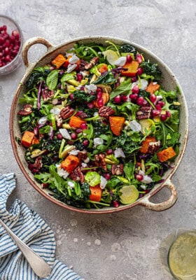 Overhead view of Christmas salad with massaged kale, arugula, Brussels sprouts, roasted sweet potatoe chunks and pomegranate seeds in a round serving bowl.