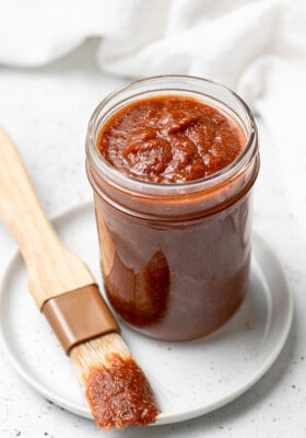 45 degree shot of homemade barbecue sauce in a medium glass jar with a brush