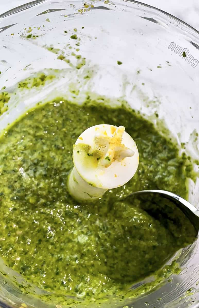 Blended basil pesto in a food processor with a spoon