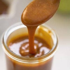 Caramel sauce in glass container with spoon.