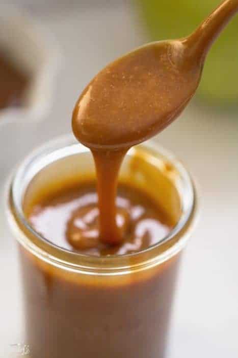 Caramel sauce in glass container with spoon.